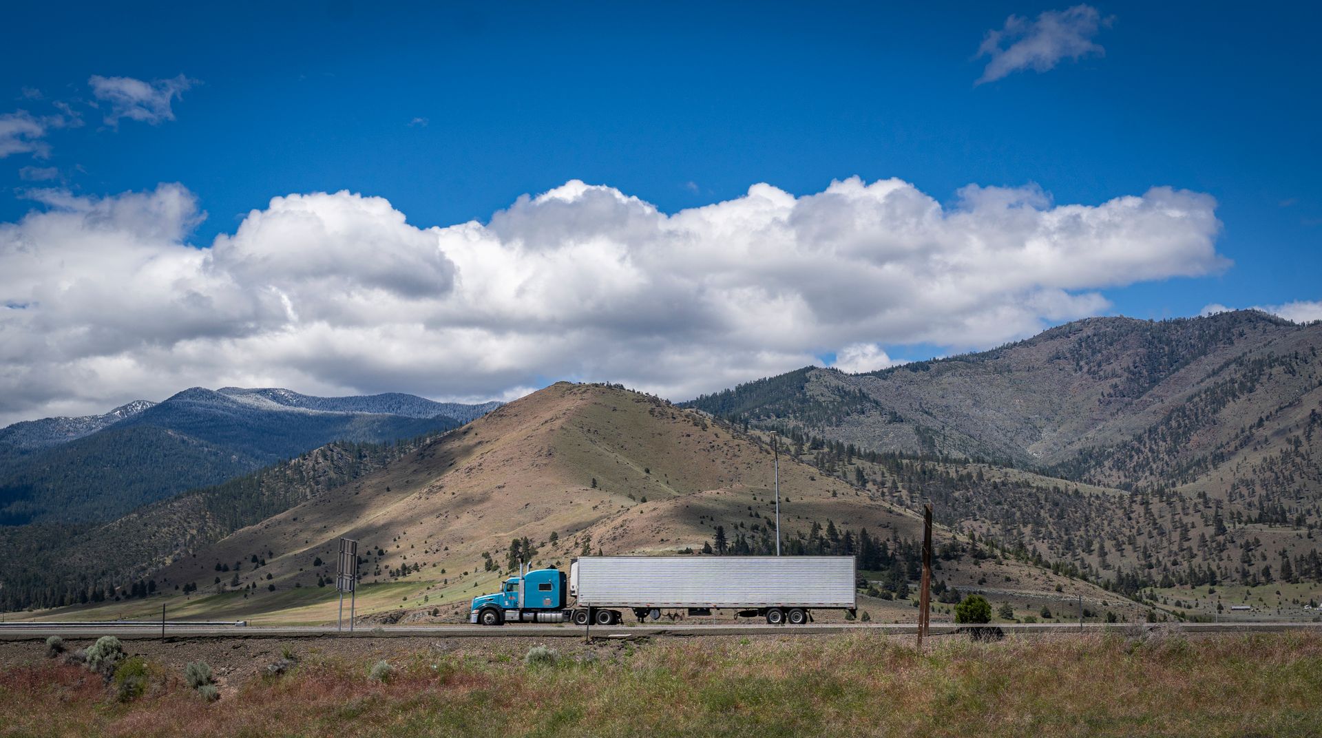 Semi truck hauling a trailer along a mountain highway under a blue sky